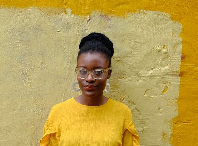 woman in yellow crew neck long sleeve shirt leaning on yellow painted wall